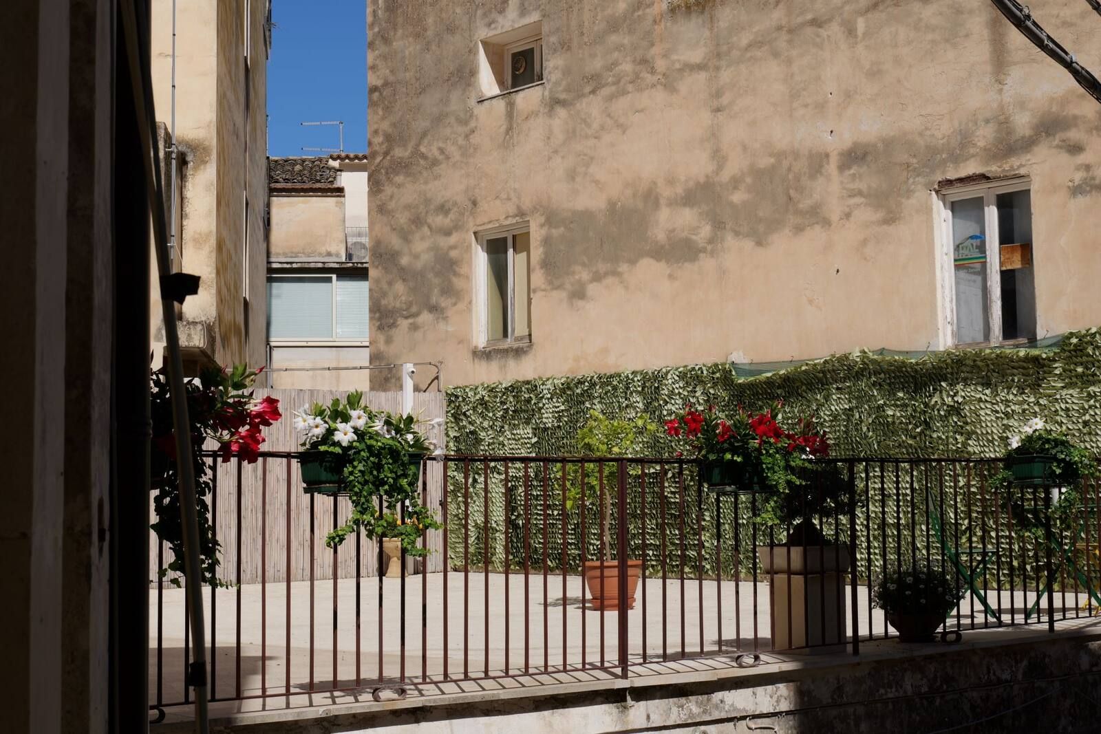 La ringhiera del balcone con i vasi di fiori e le case del vicolo