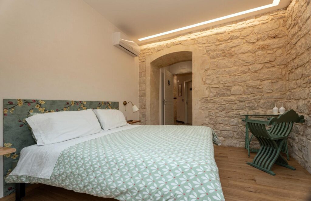 Camera Idria: letto matrimoniale, testiera verde e parete in pietra