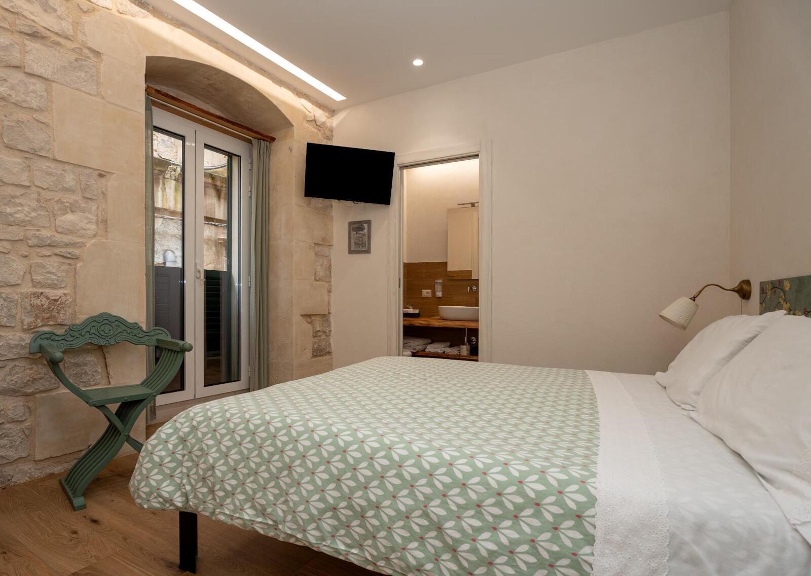 Camera Idria: letto matrimoniale, parete in pietra e porta sul balcone