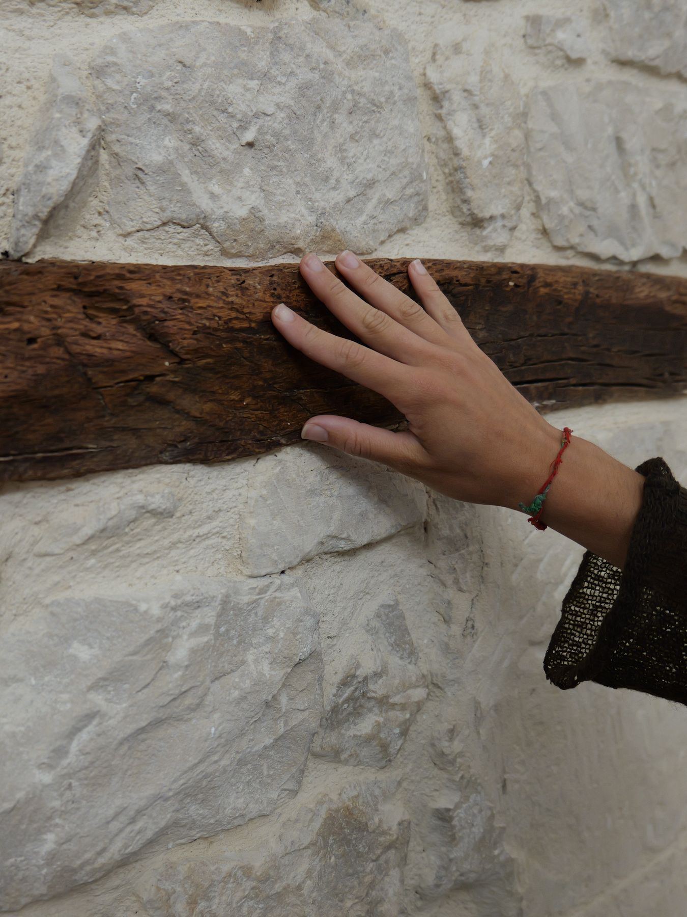 Una mano sulla trave antica incastonata nella parete in pietra